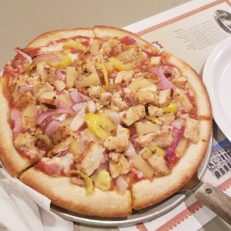 A Fursty's Restaurant pizza with chicken, pineapple, red onion, and yellow peppers on a metal pan.