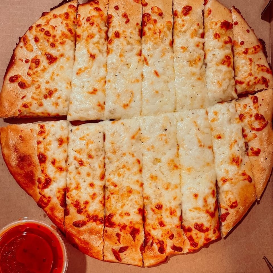 Fursty's cheesy breadsticks, cut into strips, with a side of marinara sauce in a take-out box.