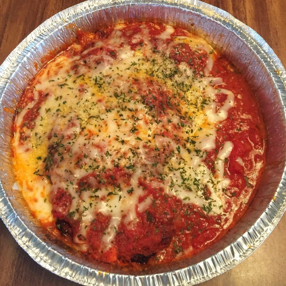 A baked dish with melted cheese, red sauce, and herbs in a foil pan from Fursty's Restaurant.