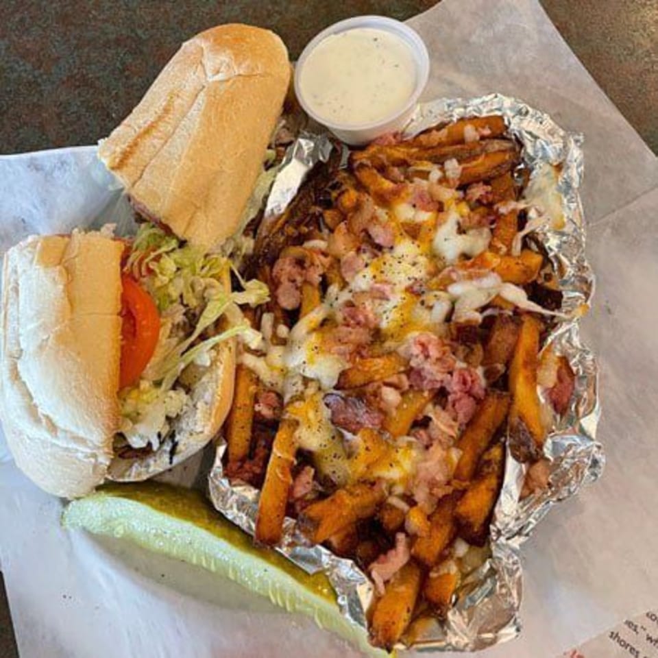 A sub sandwich, loaded fries with cheese and bacon, a side of ranch, and a pickle.