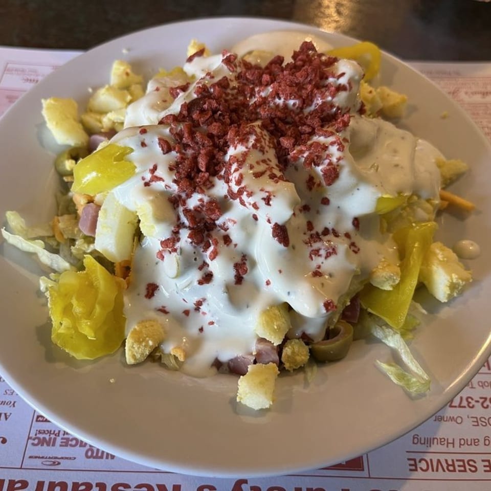 A close-up of a Fursty's Restaurant salad with white dressing, bacon bits, and yellow peppers.